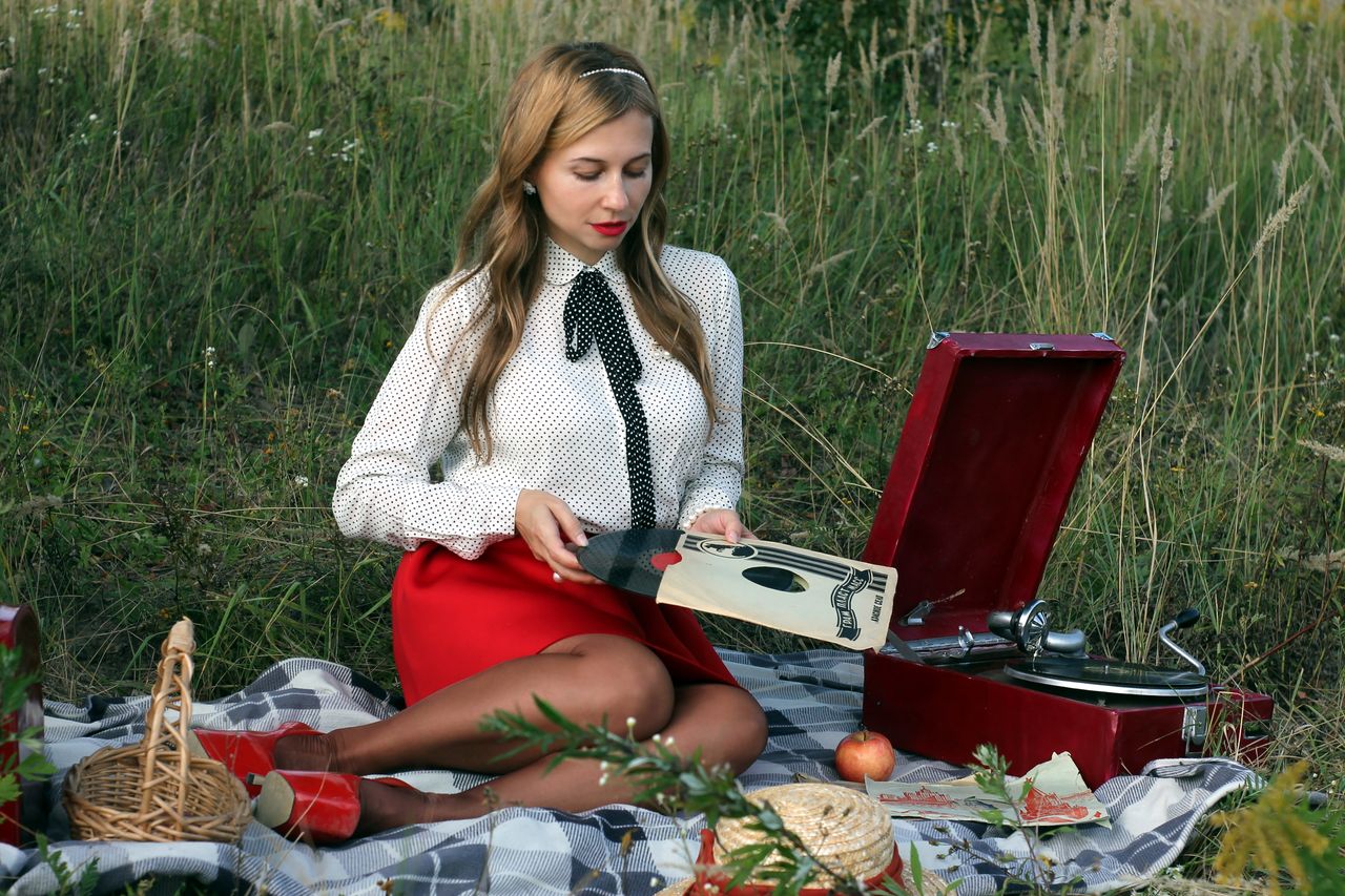 A woman enjoys a picnic with a vintage record player in a scenic outdoor setting.